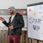 Seorang pengusaha muda mempresentasikan rencana bisnis di depan papan tulis, menggambarkan proses menemukan peluang usaha